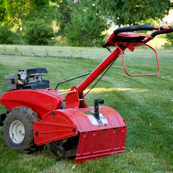 Red tiller on a grassy lawn with trees in the background