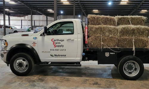 White flatbed truck with hay bales on the back in a warehouse setting