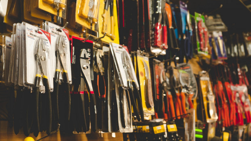 A wall display in a hardware store featuring various pliers and tools in plastic packaging. Tools are organized by size and type, creating a colorful and organized scene.